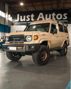 Sand Toyota 70 Series troop carrier under Just Autos banner